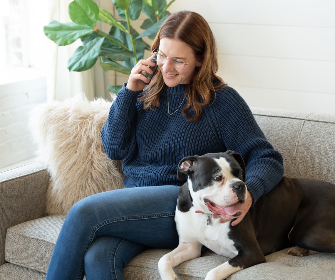 MacKenzie speaking on the phone, with Dottie next to her on a couch