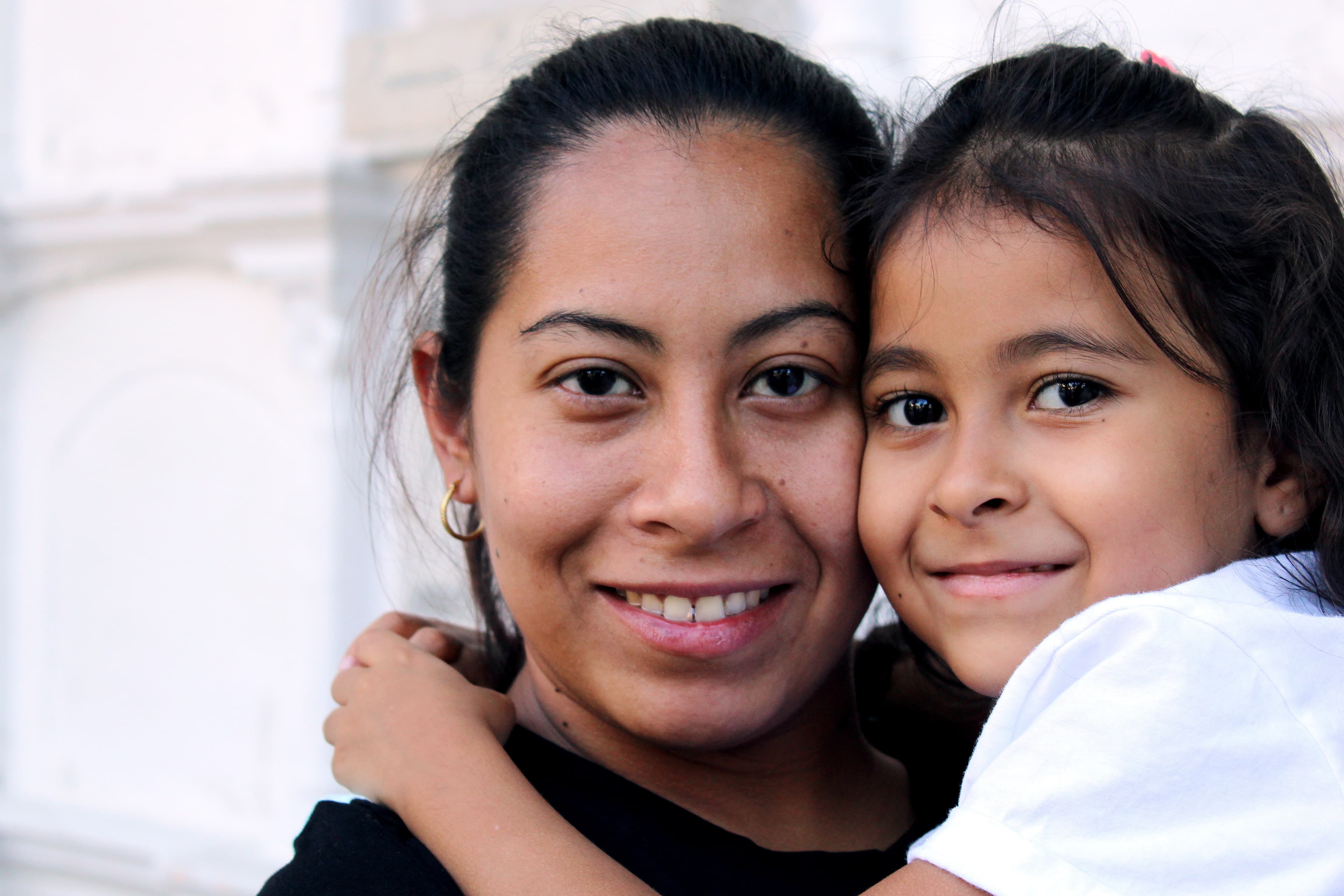 A Latino woman with her young child, smiling at the camera